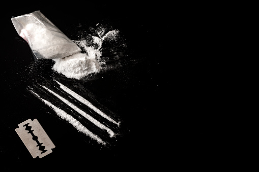 Drug addiction and substance abuse concept theme with lines of cocaine, a small bag with white powder and a blade used to cut each line of narcotics on a dark mirror table with copy space