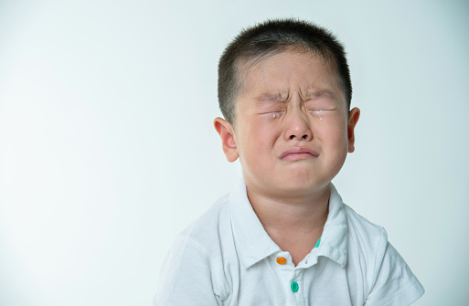 Asian boy crying against white background.