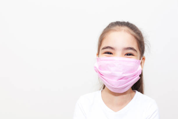 Smilling little girl with mask on the grey light background in the studio.