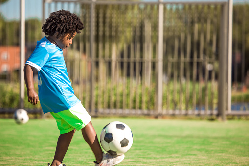 A young black boy child playing soccer on a neighbourhood football pitch on a beautiful sunny day in the Netherlands