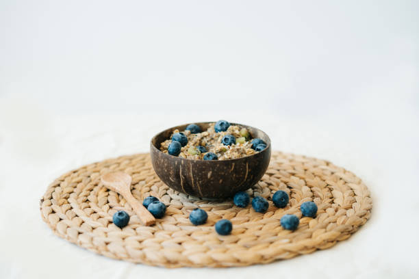 oatmeal porridge in bowl with fresh blueberries.Healthy vegan Breakfast cereals, against background of brown natural seaweed napkin and natural wooden bamboo spoon.Concept of clean food gachas de avena en un tazón con arándanos frescos. cereales saludables veganos para el desayuno, contra el fondo de la servilleta de algas marinas naturales marrones, cuchara de bambú de madera natural. concepto de comida limpia, estilo de vida saludabl