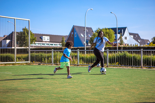 An african american father and mother with young sons playing soccer on a neighbourhood football pitch on a beautiful sunny day in the Netherlands