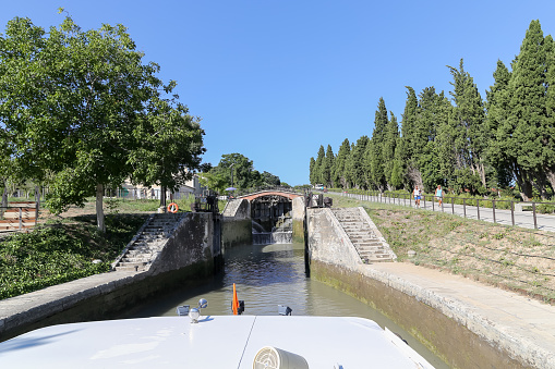 Beziers, Herault, France - August 20 2018: Looking towards the rushing water from the first lock of 9 at Les 9 Ecluses de Fonseranes with people walking along the pathway near the entrance to the locks