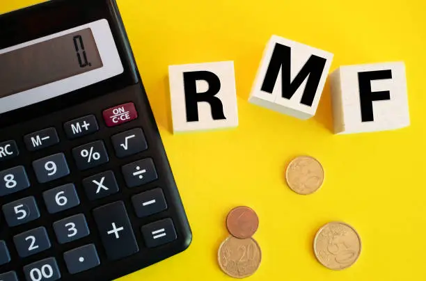 Text RMF for Retirement Mutual Fund made from wooden blocks with pile of coins spilling out of glass piggy bank on table with copy space. Taxation, and investment planing concept