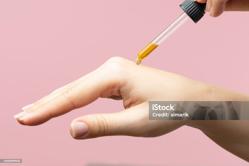 Skin Care Hand is about to receive a drop of skincare serum in front of pink background. Essential Oil Stock Photo