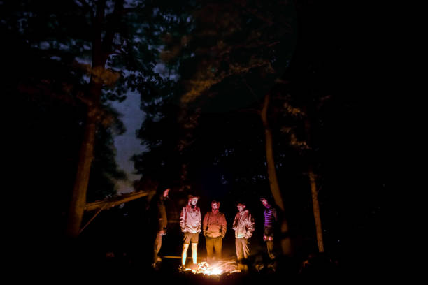Group of men, backpackers, tourist standing around campfire in forest under oak trees and sky is visible between trees White Carpathians in Czechia (Carpathian mountain range) stock photo
