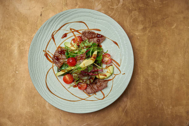 istock Salad with grilled beef, arugula, cherry tomatoes, avocado in a white ceramic plate on a copper, metal background. Close up. Warm meat salad 1240136302