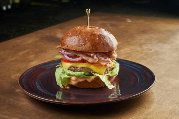 istock Appetizing and juicy burger with beef, tomato, onion, lettuce, bacon and melted cheese in a dark ceramic plate on a copper, metal background 1240138846