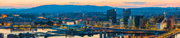 Orange glow of midsummer sunset over the iconic landmarks and waterfront of central Oslo to the forested hills of southern Norway beyond.