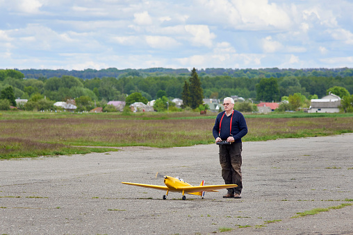 An elderly man launches a radio-controlled aircraft on the runway in the spring.