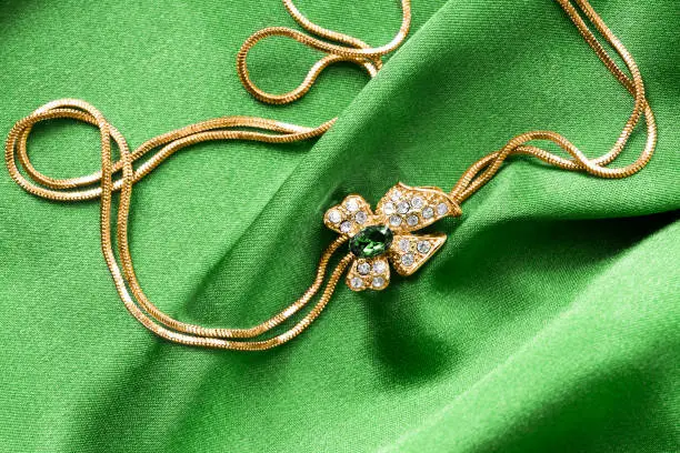 Gold necklace with a bow shaped pendant with crystals on green satin background