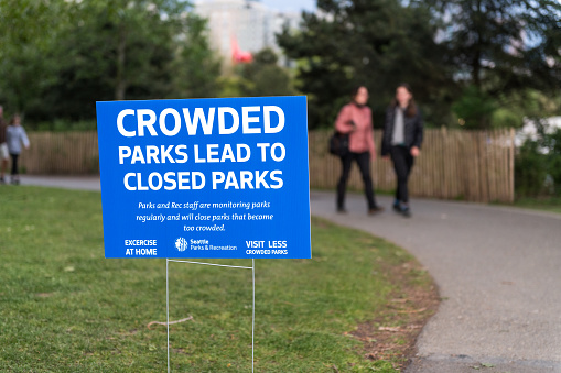 Seattle, USA - Apr 26th, 2020: Late in the day people enjoying Myrtle Edwards Park during the covid-19 pandemic. With a warning sign from the city about crowding.