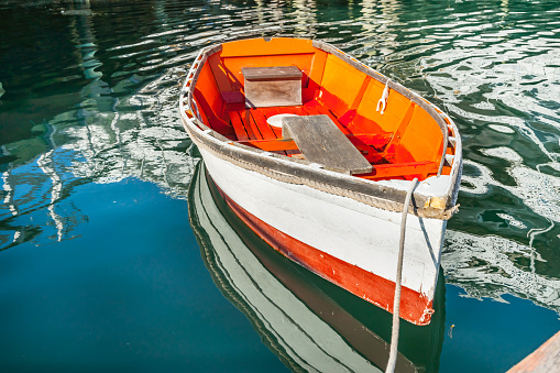 Bright orange and white painted wooden dinghy tied to pier at Boothbay town and harbor, Maine USA.