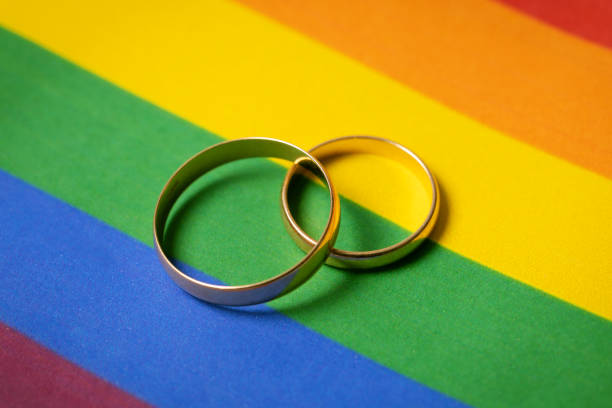 gleichgeschlechtliche ehe konzept - zwei eheringe auf lgbt regenbogen-flagge - schwulenehe stock-fotos und bilder