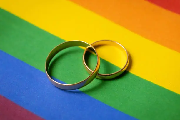 Photo of same-sex marriage concept - two wedding rings on lgbt rainbow flag