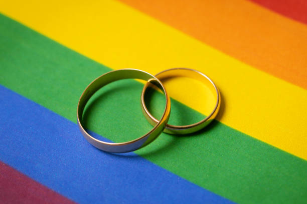 однополые браки концепции - два обручальных кольца на lgbt радужный флаг - married стоковые фото и изображения