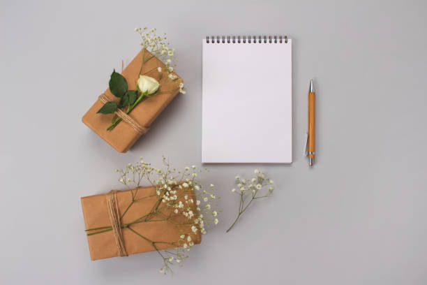 istock Beautiful vintage flat lay minimal composition with wooden pen, notebook and gift boxes wraped with kraft paper with tiny gypsophila Baby's-breath flowers and roses on grey background with copy space 1240204933