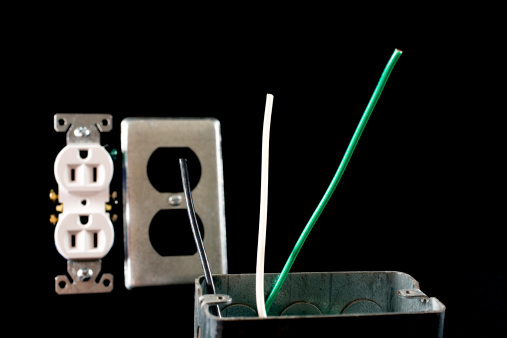 Electrical plug box with black, white and green wires.  Plug and cover is soft focus in background.