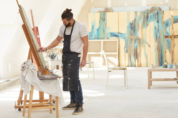 istock Male Artist Painting on Easel in Workshop 1240227657