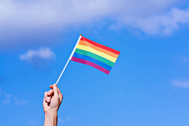 Annual LGBT Pride month Celebration in June Raised hand with waving LGBTQ rainbow flag against blue sky. Annual LGBT Pride Celebration rainbow flag photos stock pictures, royalty-free photos & images