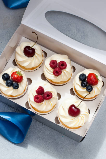 istock Cupcakes with whipped cream, fresh cherries, raspberries, blueberries, strawberries in gift box with blue ribbon. 1240253499