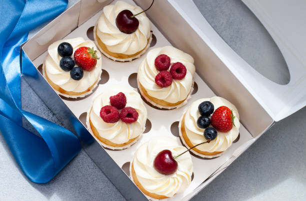 istock Cupcakes with whipped cream, fresh cherries, raspberries, blueberries, strawberries in gift box with blue ribbon. 1240253515