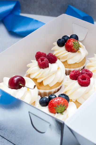 istock Cupcakes with whipped cream, fresh cherries, raspberries, blueberries, strawberries in gift box with blue ribbon. 1240253748