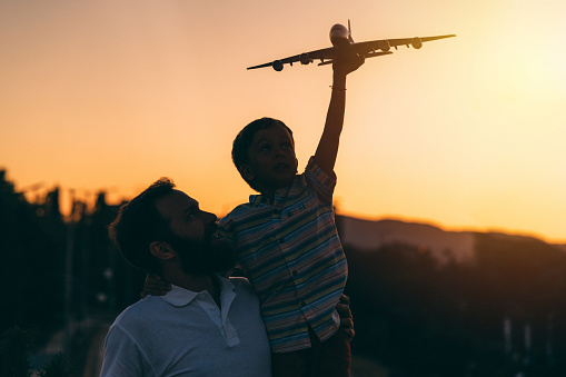 Single father playing with his son outside, flying with model airplane