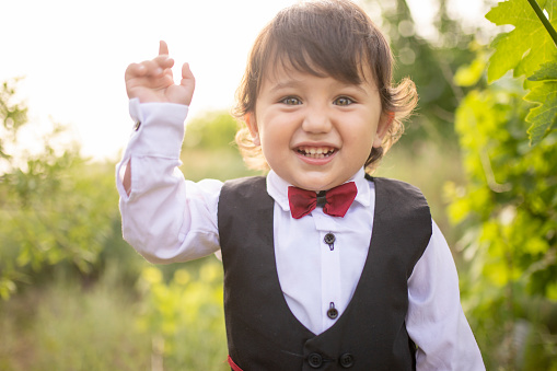 Portrait of little boy in suit against color background. make hand sign.