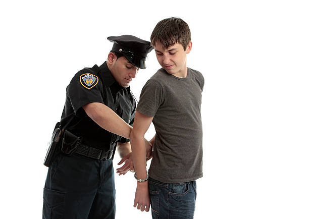 Policeman handcuffing teenager A police officer arrests and handcuffs a young male teen felon. child arrest stock pictures, royalty-free photos & images