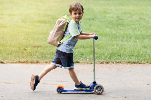 istock Smiling schoolboy running to school in a scooter carrying a backpack 1240383466