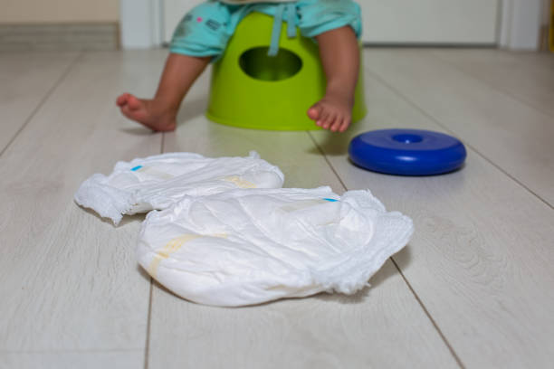 potty training concept. close-up a diaper lies on a white floor, in the background a cute little baby sits on a green pot with toy in the room in blur. soft focus stock photo