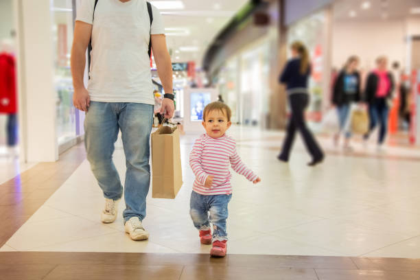 Black friday sale concept, shopping with children. little cute girl is walking along the mall with dad with a craft paper bag for shopping. close-up, soft focus, blur background stock photo
