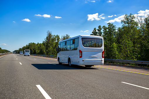 three new white minibuses ride in a convoy along the highway on a sunny day in summer. close up, back view