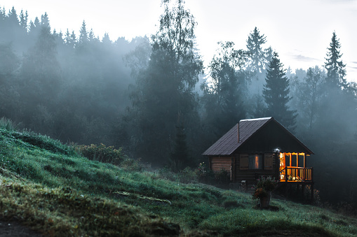 Small old wooden house in foggy forest. Mountains scenery. Nature conceptual image