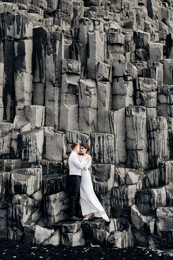 Una pareja de bodas se para en una pared de pilares de piedra. Los novios se abrazan en kekurs de basalto, en la playa de arena negra de Vik. Destino boda islandia. photo