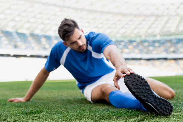 istock selective focus of professional soccer player in blue and white uniform stretching on football pitch at stadium 1240469194
