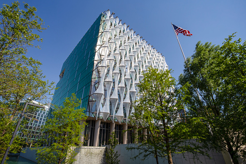 An ultra wide angle view of the US Embassy with the American flag in the foreground. London, England - 1 June 2020.