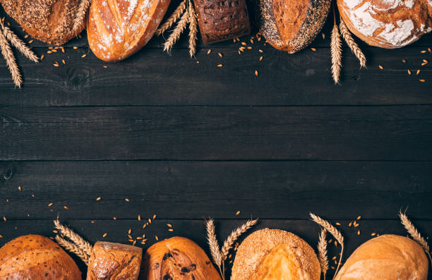 istock Bread border on wood background with copy space. Vertical composition of whole grain loaves with ears. Different kinds of bread. Bakery, cooking and grocery store concept. 1240507716