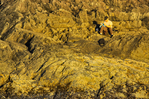 Younger male resting on beach rocks along the shoreline of Pacific Rim National Park on Vancouver Island, British Columbia