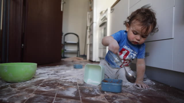 Toddler boy having fun with flour at kitchen