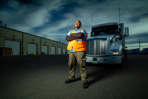 Dramatic portrait shot with strobes of a truck driver wearing a hi-vis vest posing by his truck.