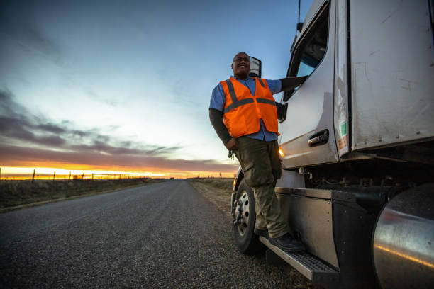Truck Driver on Steps of Cab Looking Into Distance on Country Road Dramatic portrait shot with strobes of a truck driver wearing a hi-vis vest posing by his milk tanker on a country road at sunset. semi truck photos stock pictures, royalty-free photos & images