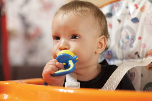 a small child eats with a spoon and sits and holds the edge of the feeding table in the nursery, grimy and stained with food, baby food concept, complementary foods, the first spoon, nibbler, fruit feeder pacifier un niño pequeño come con una cuchara y se sienta y sostiene el borde de la mesa de alimentación en el vivero, sucio y manchado con alimentos, concepto de comida para bebés, alimentos complementarios, la primera cuchara, mordisqueador, alimentador de fr