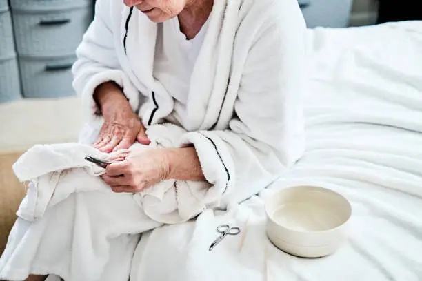 Mature woman in bedroom nail care treatment