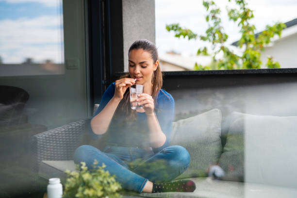 fille s’asseyant sur le balcon et mangeant des pillules nutritionnelles de supplément - water women glass healthy eating photos et images de collection