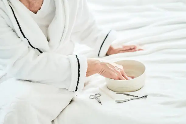 Mature woman in bedroom nail care treatment