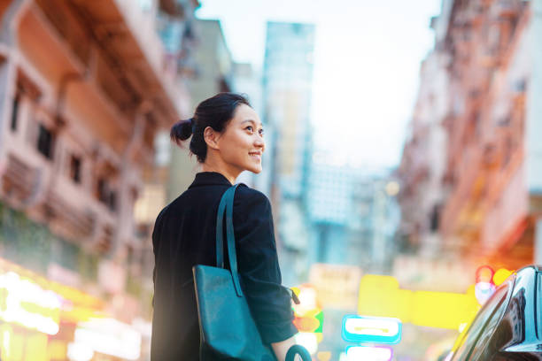 Rear view of young Chinese businesswoman standing by car looking away in Hong Kong Rear view of young Chinese businesswoman standing by car looking away in Hong Kong’s Yau Ma Tei and Jordan areas women satisfaction decisions cheerful stock pictures, royalty-free photos & images