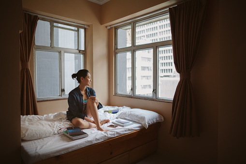 Asian woman sit on bed looking though window in Hong Kong’s Yau Ma Tei and Jordan areas