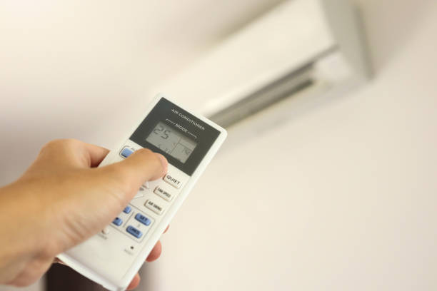istock Hand with remote control directed on air conditioner inside the room 1240649009